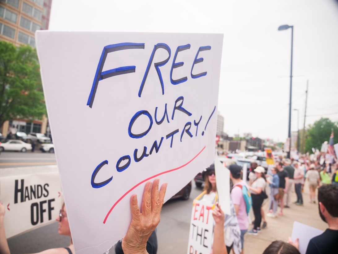 En protestskylt med texten 'FREE OUR COUNTRY!' hålls upp under en demonstration.