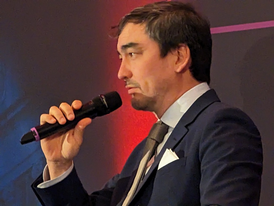 En finansiell expert i kostym talar i en mikrofon på ett företagsevent.